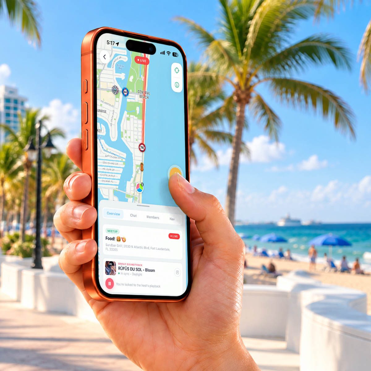 A hand holding an iPhone on Fort Lauderdale beach, thumb pressing Caravan’s amber Chirp push-to-talk button over a live map with friends’ pucks and a route along the coast.