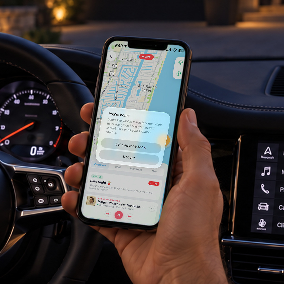 A driver parked at home at night holding an iPhone: Caravan showing the “You’re home” prompt, offering to let the group know they arrived safely and end location sharing.